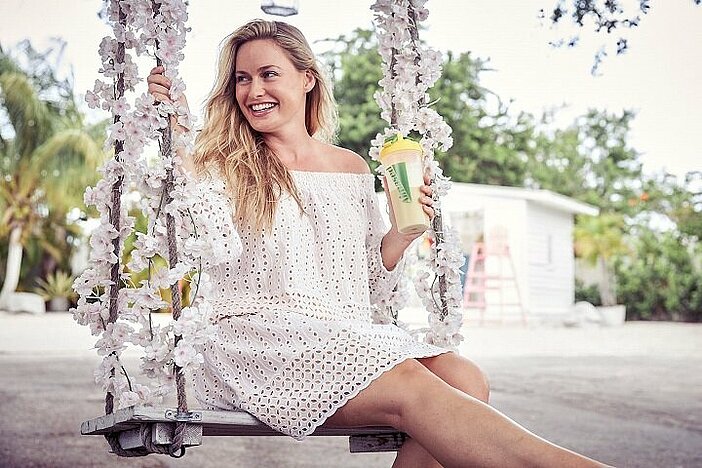 Blonde girl in white dress sitting on a swing with Almased shake because research shows it reduces hunger.